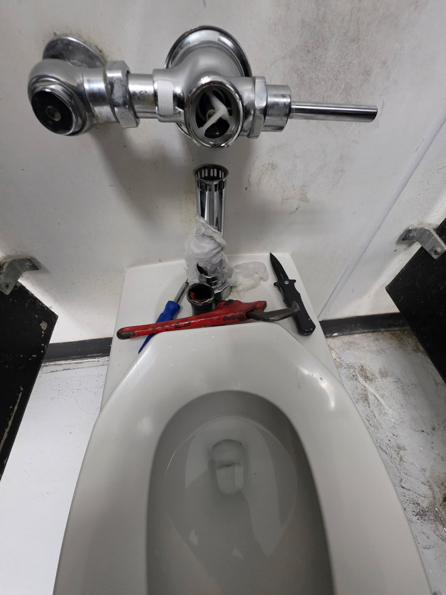 Commercial toilet flush valve repair with plumbing tools on the fixture