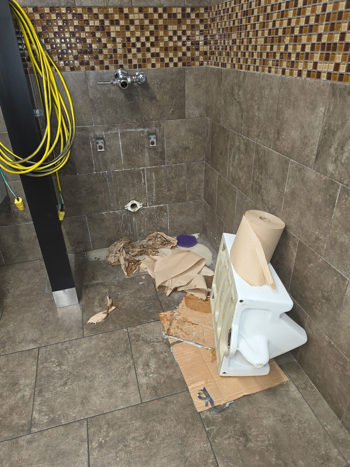 Commercial urinal removed from a tiled restroom wall during plumbing work