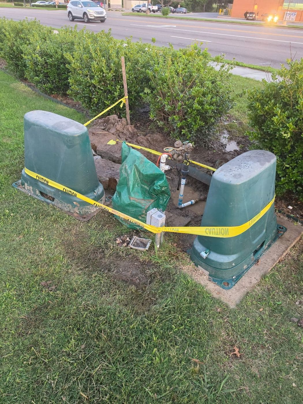 Outdoor backflow assembly with green protective covers and yellow caution tape